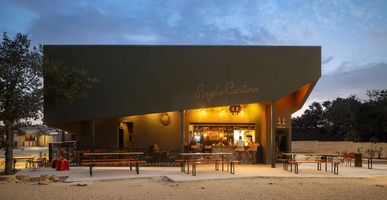 Singhs Cantina exterior at dusk with lit bar and patio picnic tables, San Antonio